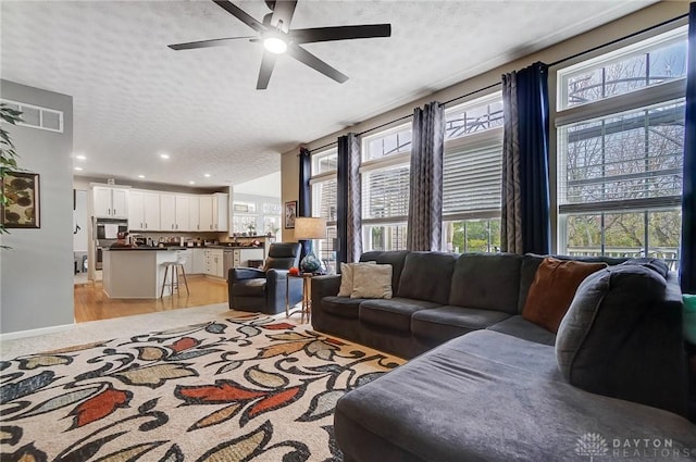 living room featuring ceiling fan, a healthy amount of sunlight, light wood-type flooring, and a textured ceiling