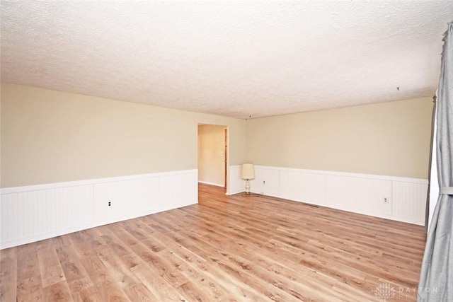 empty room with wainscoting, a textured ceiling, and light wood finished floors