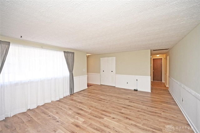 spare room with light wood-style floors, wainscoting, and a textured ceiling