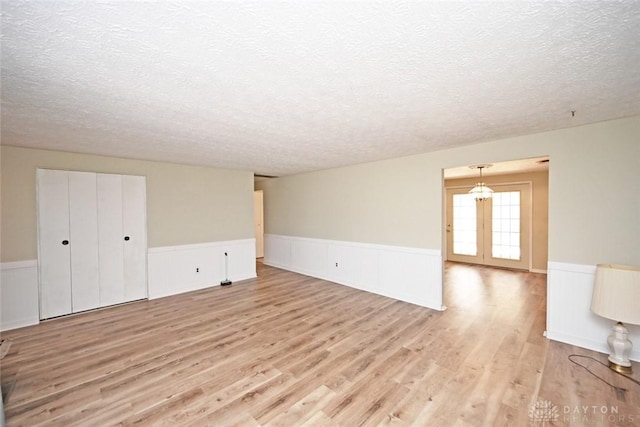 unfurnished room with light wood-type flooring, a wainscoted wall, and a textured ceiling