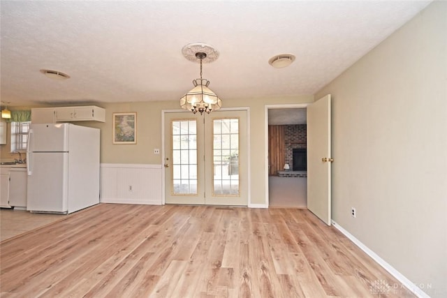 unfurnished dining area with wainscoting, a textured ceiling, light wood-style floors, a fireplace, and a chandelier