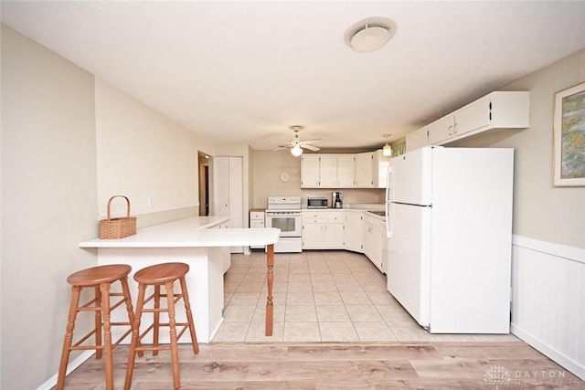 kitchen with white appliances, a kitchen breakfast bar, a peninsula, light countertops, and white cabinetry