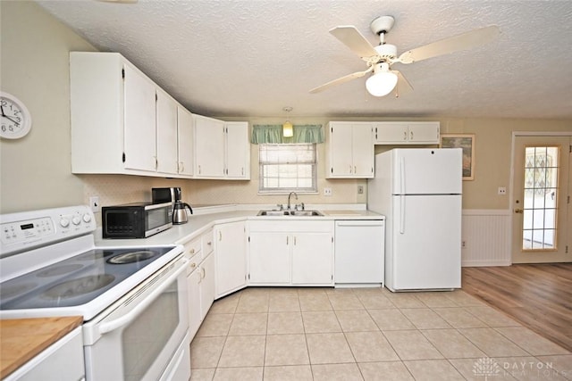 kitchen featuring a wainscoted wall, light countertops, white cabinetry, a sink, and white appliances