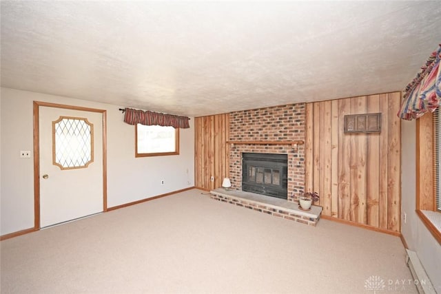 unfurnished living room with a textured ceiling, wooden walls, carpet floors, baseboards, and a brick fireplace