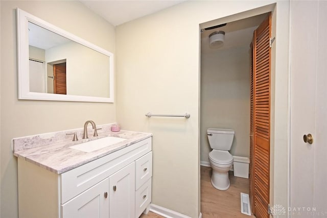 bathroom featuring baseboards, visible vents, toilet, wood finished floors, and vanity