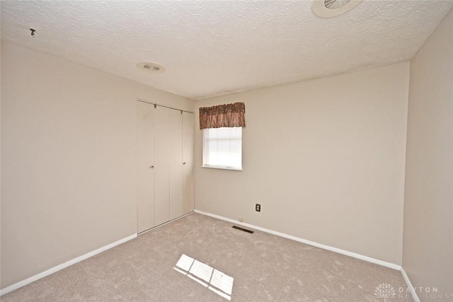 spare room featuring carpet, a textured ceiling, visible vents, and baseboards