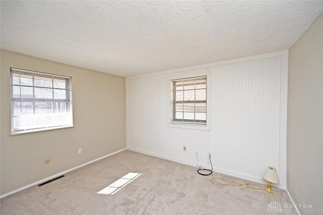 carpeted empty room featuring a wealth of natural light, visible vents, and a textured ceiling