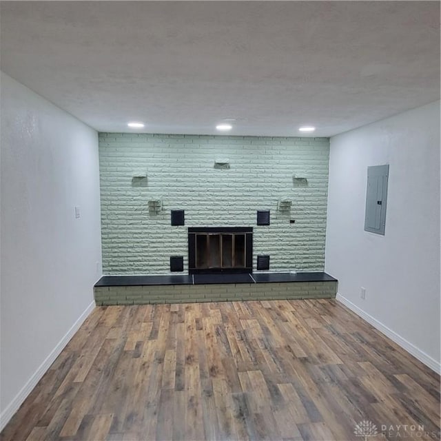 unfurnished living room with electric panel, hardwood / wood-style floors, a fireplace, and brick wall