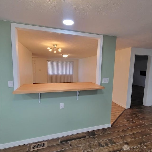 kitchen with a kitchen bar, kitchen peninsula, dark wood-type flooring, and a textured ceiling