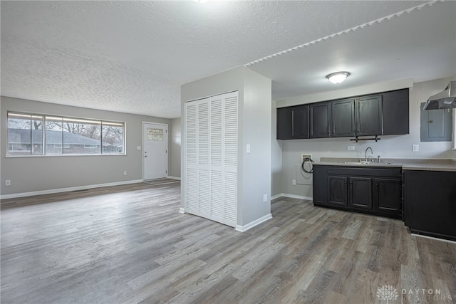 kitchen with sink, wall chimney range hood, a textured ceiling, and light hardwood / wood-style flooring