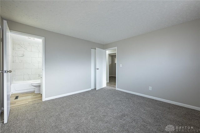 unfurnished bedroom with ensuite bath, a textured ceiling, and carpet flooring