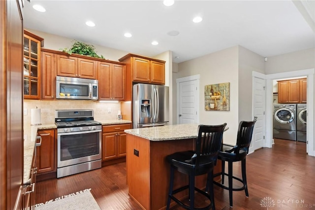 kitchen with washing machine and clothes dryer, a center island, stainless steel appliances, light stone counters, and dark hardwood / wood-style floors