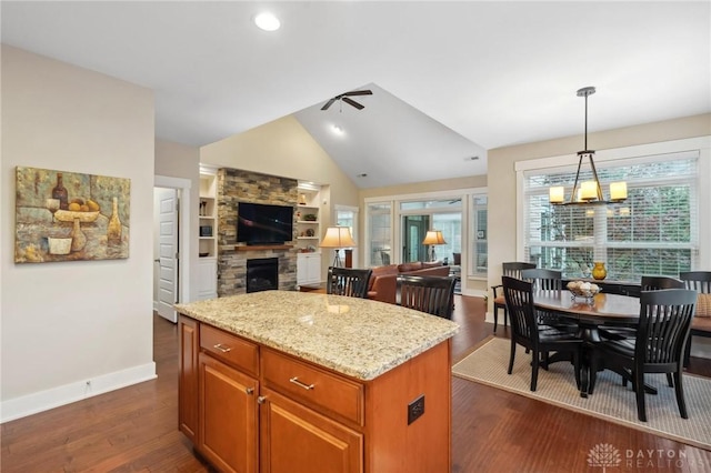 kitchen with pendant lighting, a center island, dark wood-type flooring, ceiling fan with notable chandelier, and light stone countertops