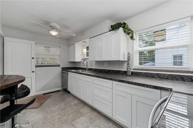 kitchen featuring white cabinets, sink, stainless steel dishwasher, ceiling fan, and dark stone countertops