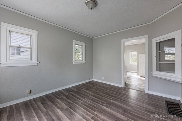 spare room featuring a healthy amount of sunlight, ornamental molding, and dark wood-type flooring