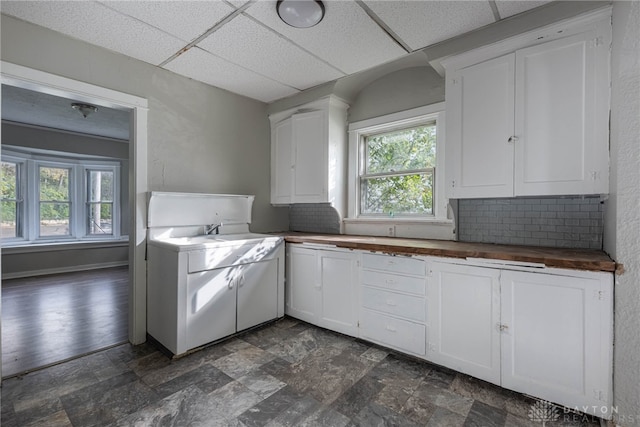 kitchen with decorative backsplash, butcher block countertops, white cabinetry, and a drop ceiling