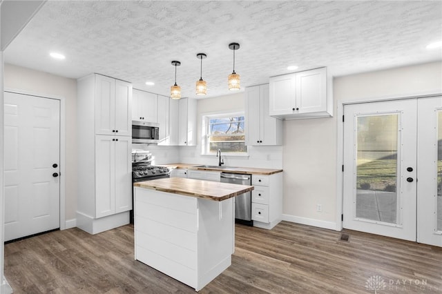 kitchen with butcher block countertops, white cabinetry, stainless steel appliances, and decorative light fixtures