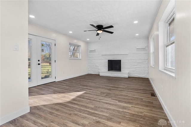 unfurnished living room featuring dark wood-type flooring, a stone fireplace, ceiling fan, and a healthy amount of sunlight