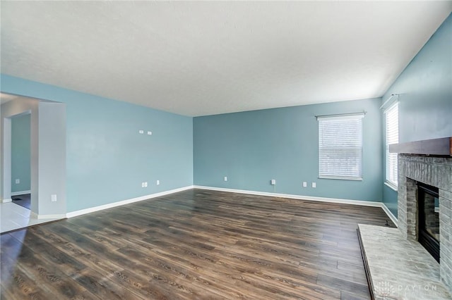 unfurnished living room with dark hardwood / wood-style flooring and a brick fireplace