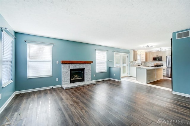 unfurnished living room with a textured ceiling, a brick fireplace, dark wood-type flooring, and sink