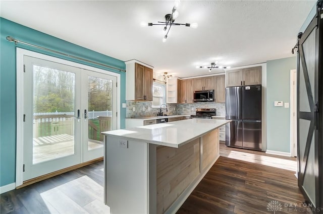 kitchen with sink, a center island, a barn door, dark hardwood / wood-style floors, and appliances with stainless steel finishes