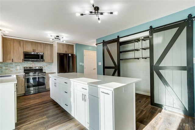 kitchen with stainless steel appliances, dark wood-type flooring, a barn door, a center island, and white cabinetry