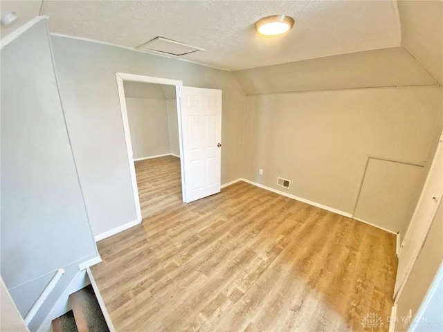 additional living space featuring a textured ceiling, light hardwood / wood-style flooring, and vaulted ceiling