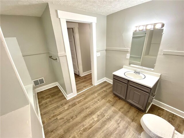 bathroom with hardwood / wood-style flooring, vanity, toilet, and a textured ceiling