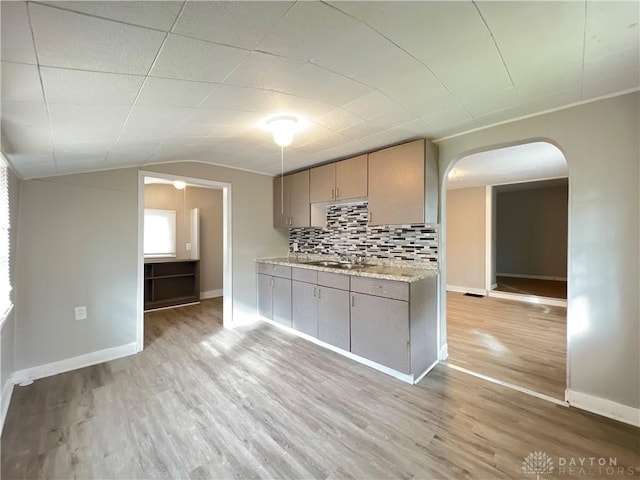 kitchen with backsplash, sink, vaulted ceiling, and light wood-type flooring