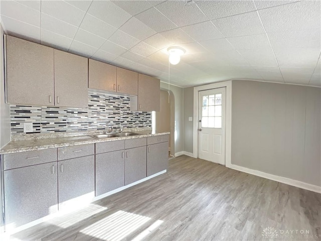 kitchen featuring backsplash, light hardwood / wood-style floors, light stone counters, and sink