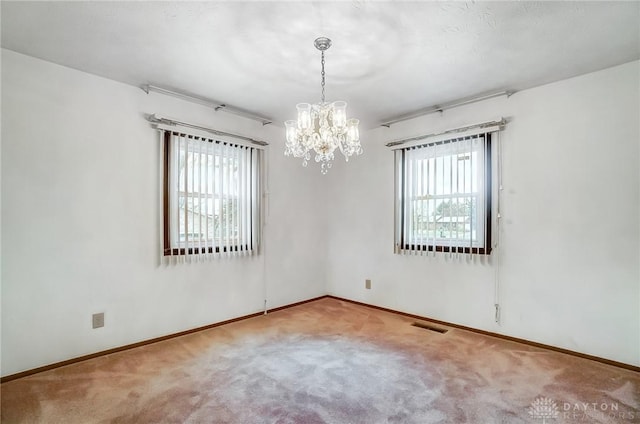 carpeted empty room featuring a wealth of natural light and a chandelier