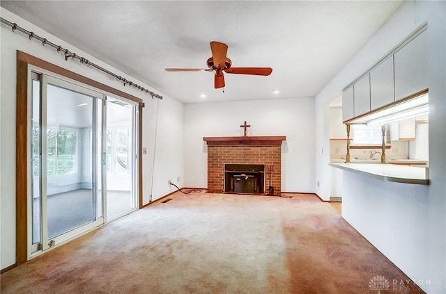 unfurnished living room featuring light colored carpet, a brick fireplace, and ceiling fan