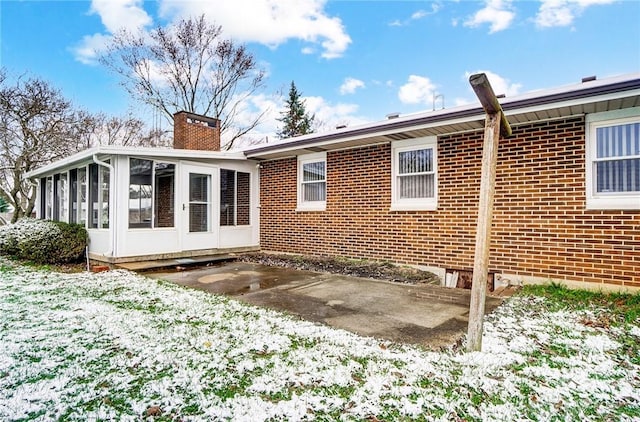 snow covered rear of property featuring a sunroom and a patio