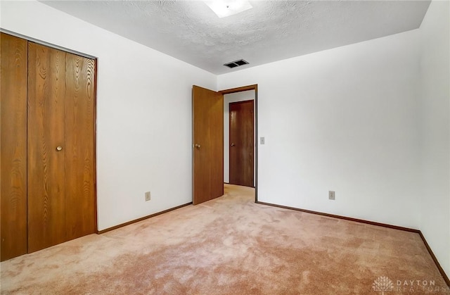 unfurnished bedroom featuring light carpet, a textured ceiling, and a closet