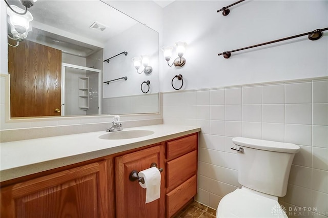 bathroom with a shower with door, vanity, tile walls, and toilet