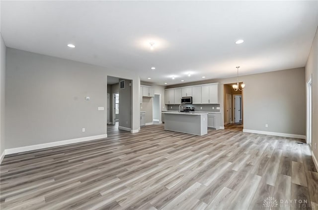 unfurnished living room with a chandelier, light hardwood / wood-style flooring, and sink