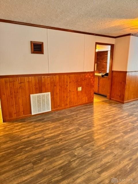 empty room with hardwood / wood-style floors, ornamental molding, a textured ceiling, and wooden walls