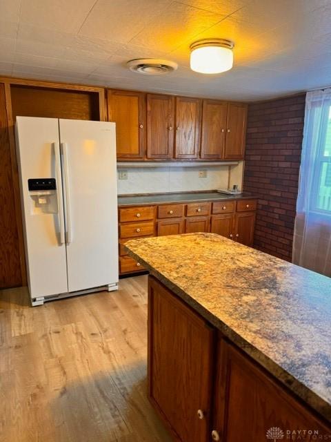 kitchen with light stone countertops, white fridge with ice dispenser, and light hardwood / wood-style flooring