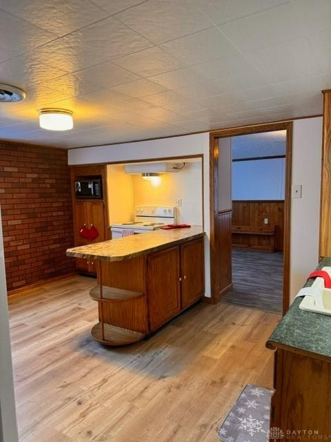 bar with white range oven, light hardwood / wood-style flooring, exhaust hood, and brick wall