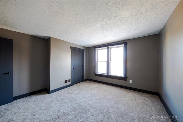 spare room featuring light colored carpet and a textured ceiling