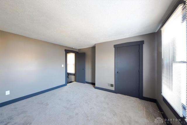 unfurnished bedroom with multiple windows, light carpet, and a textured ceiling