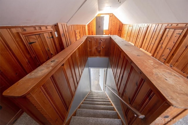 staircase with carpet, wooden walls, and vaulted ceiling