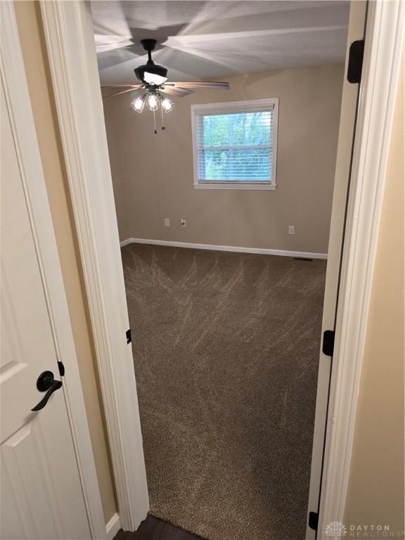 spare room featuring ceiling fan and dark colored carpet