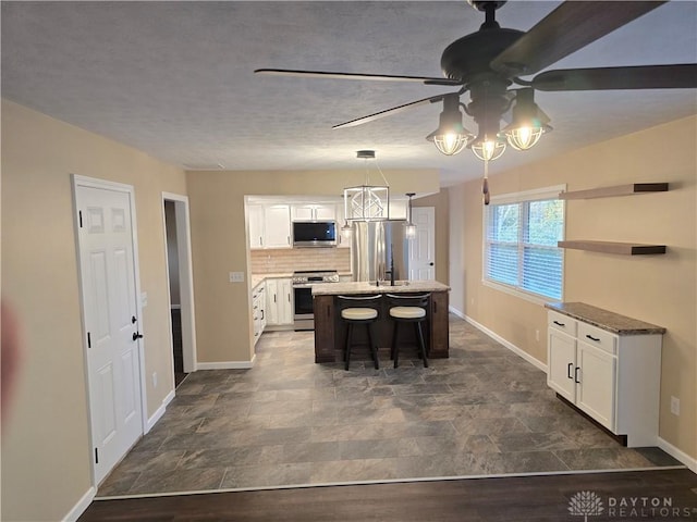 kitchen featuring a kitchen island with sink, a breakfast bar area, decorative light fixtures, white cabinetry, and stainless steel appliances