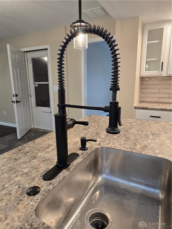 room details with backsplash, dark wood-type flooring, sink, hanging light fixtures, and white cabinetry