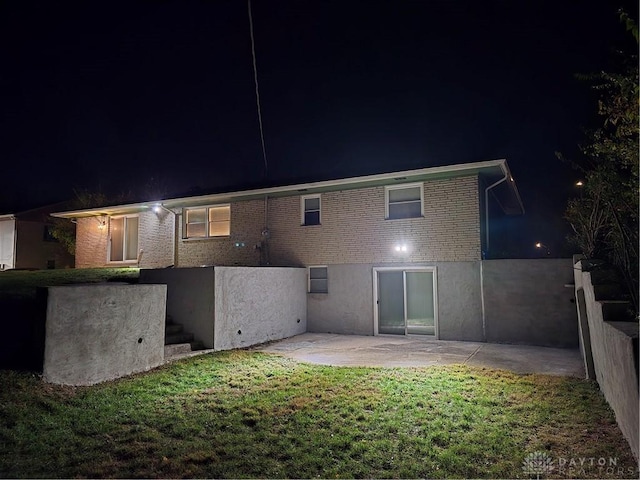 back house at night with a patio area and a lawn