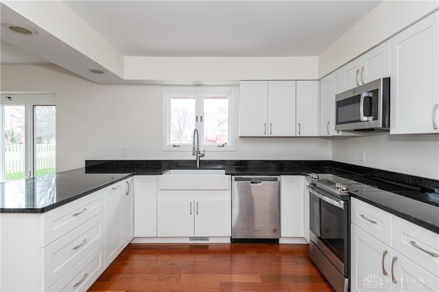 kitchen with kitchen peninsula, stainless steel appliances, sink, white cabinets, and dark hardwood / wood-style floors