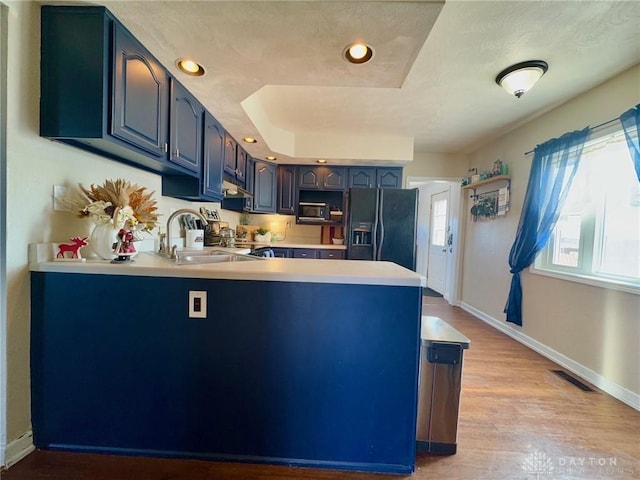 kitchen with black fridge with ice dispenser, kitchen peninsula, blue cabinets, and light wood-type flooring