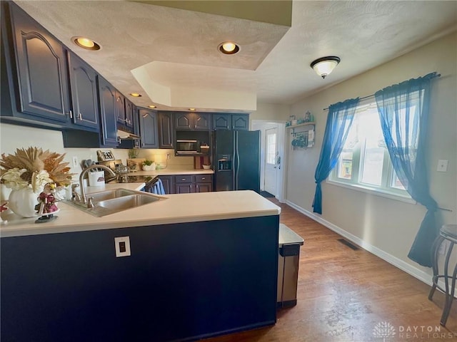 kitchen with light hardwood / wood-style floors, black fridge with ice dispenser, kitchen peninsula, and sink