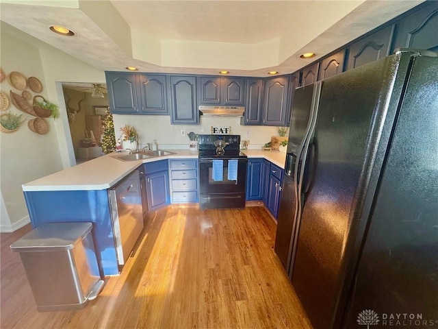 kitchen with black appliances, a raised ceiling, blue cabinets, sink, and light wood-type flooring